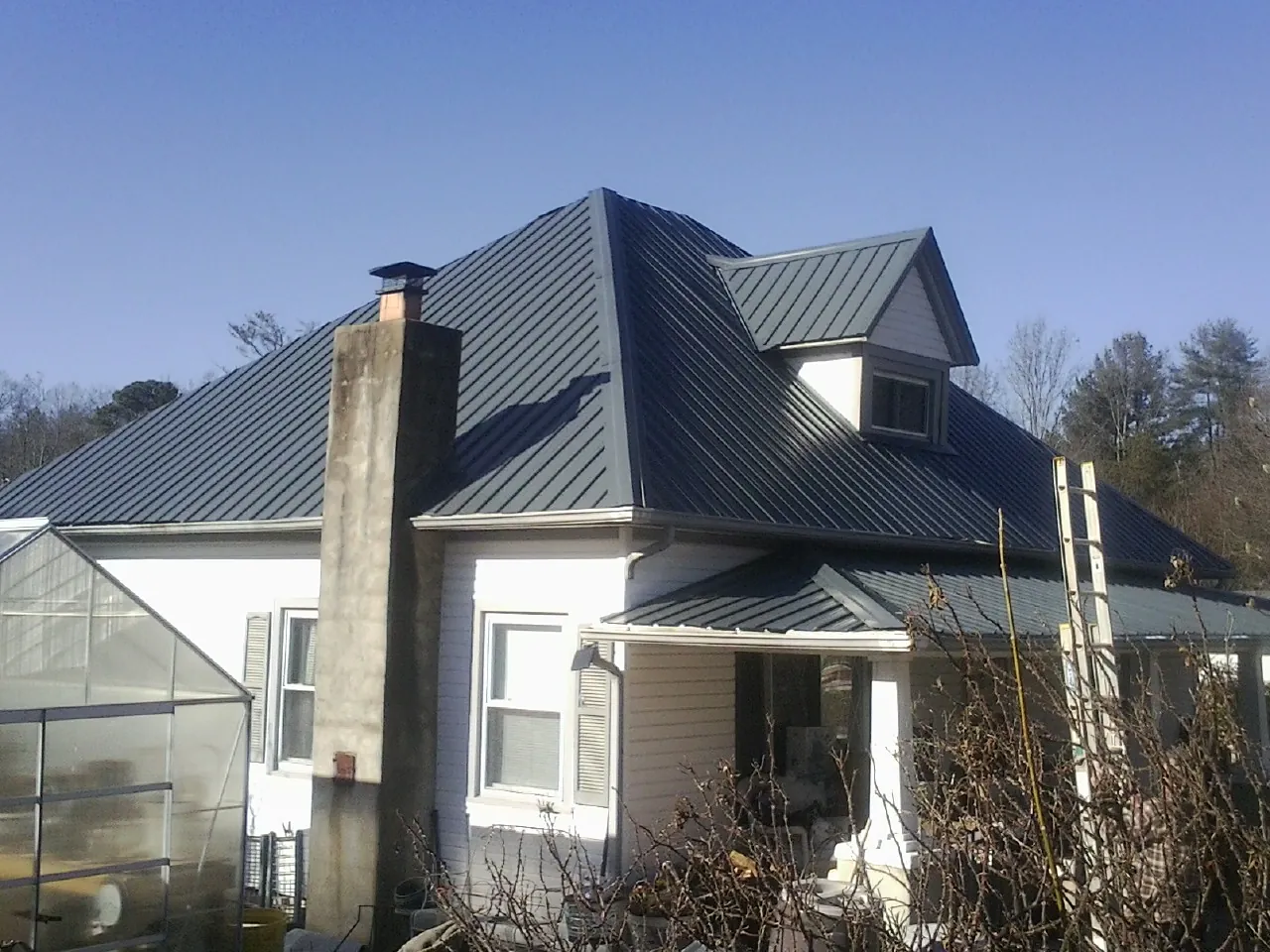 Dark blue standing seam metal roof on a white farmhouse with dormer — Slate & Tile Roof Repair by Roofing Brothers in Pebble Beach
