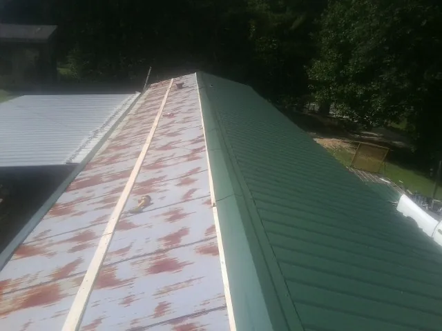 Old rusted panels beside newly installed green metal roofing — Wind Damage Roof Repair by Roofing Brothers in Pebble Beach