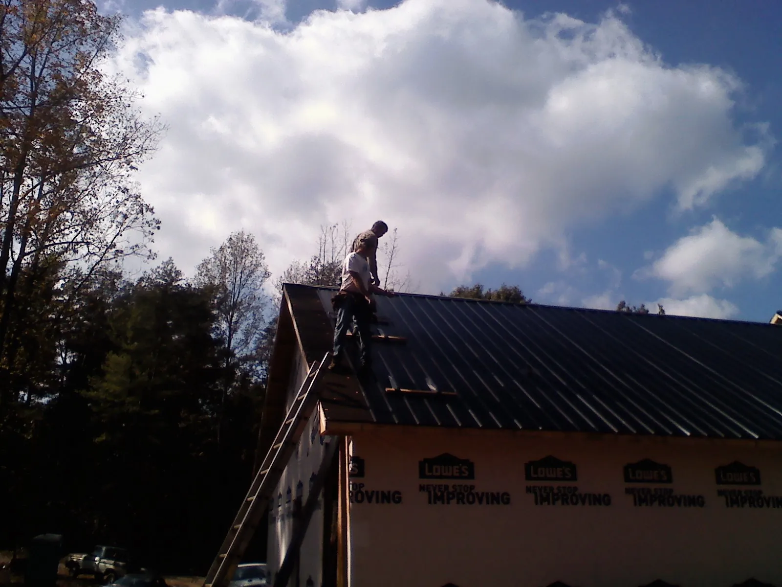 Roofer fastening dark metal panels high against a cloudy sky, from a Roof Inspection job in Pebble Beach
