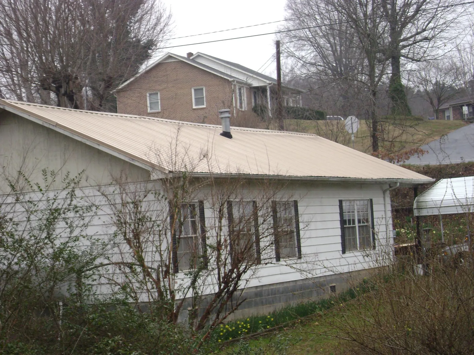 Tan metal roof on a white sided house set into a hillside — Commercial Roofing by Roofing Brothers in Pebble Beach